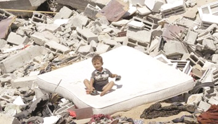 طفل يجلس فوق ركام منزل ذويه في غزة