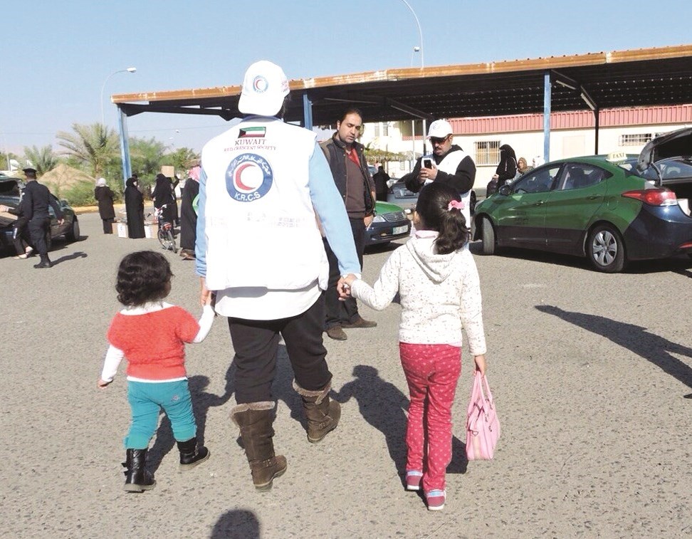 أحد المتطوعين يصطحب طفلين من اللاجئين