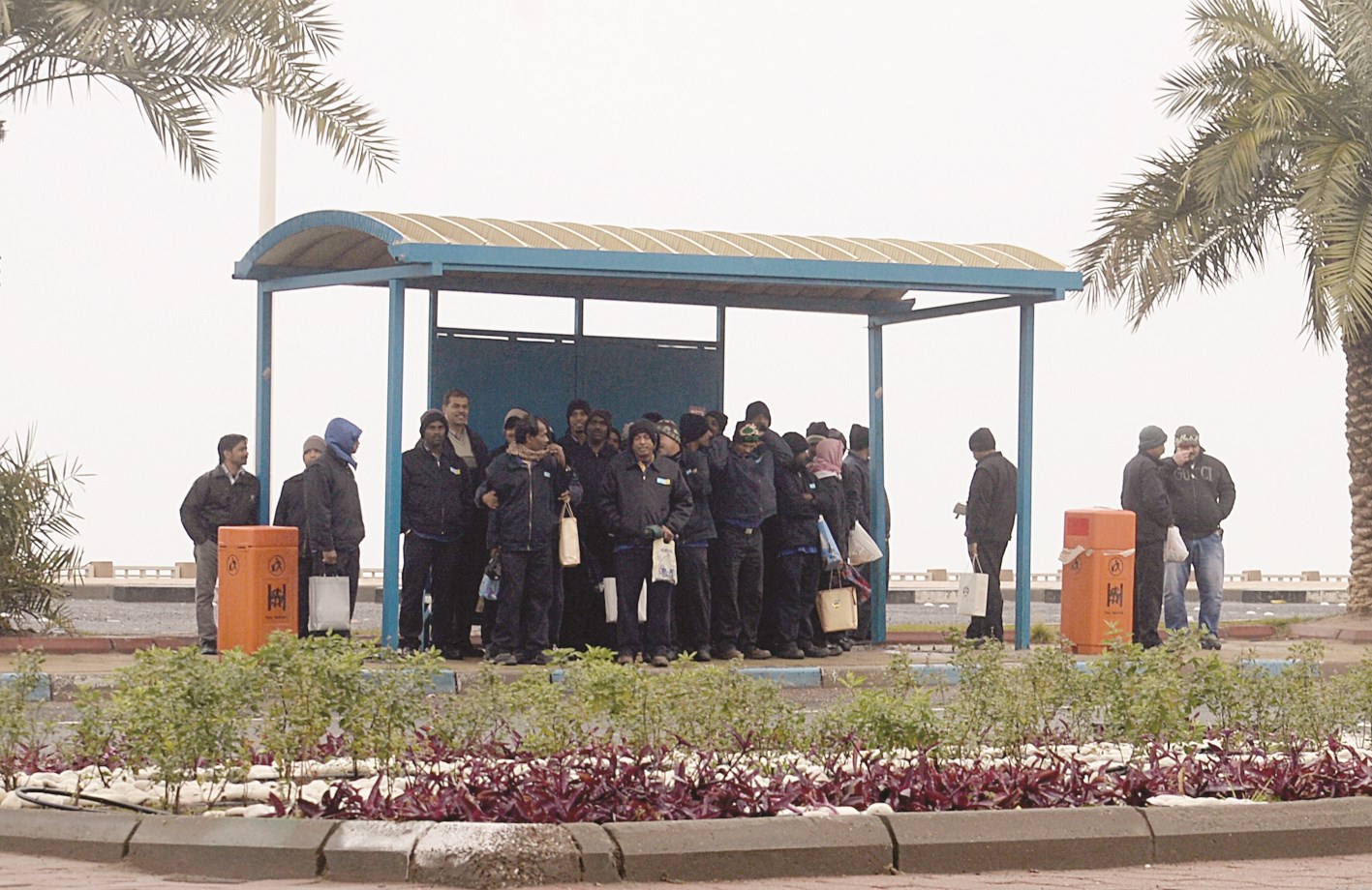 عمال لاذوا بمظلة إحدى محطات الحافلات (تصوير أسعد عبدالله)