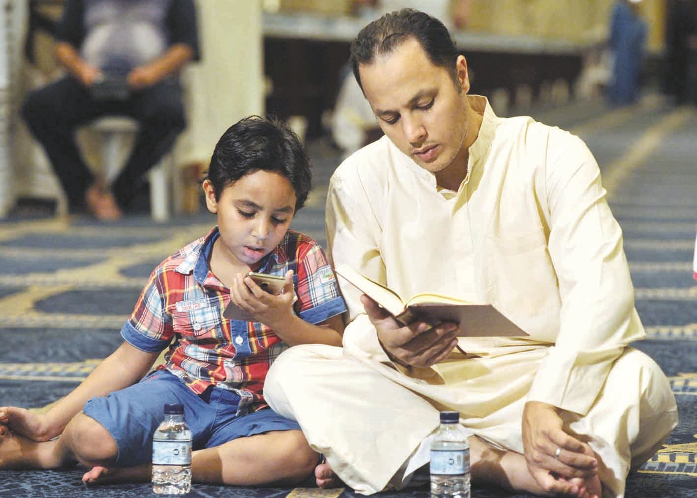 أب وإلى جواره ابنه يتلو القرآن من الهاتف