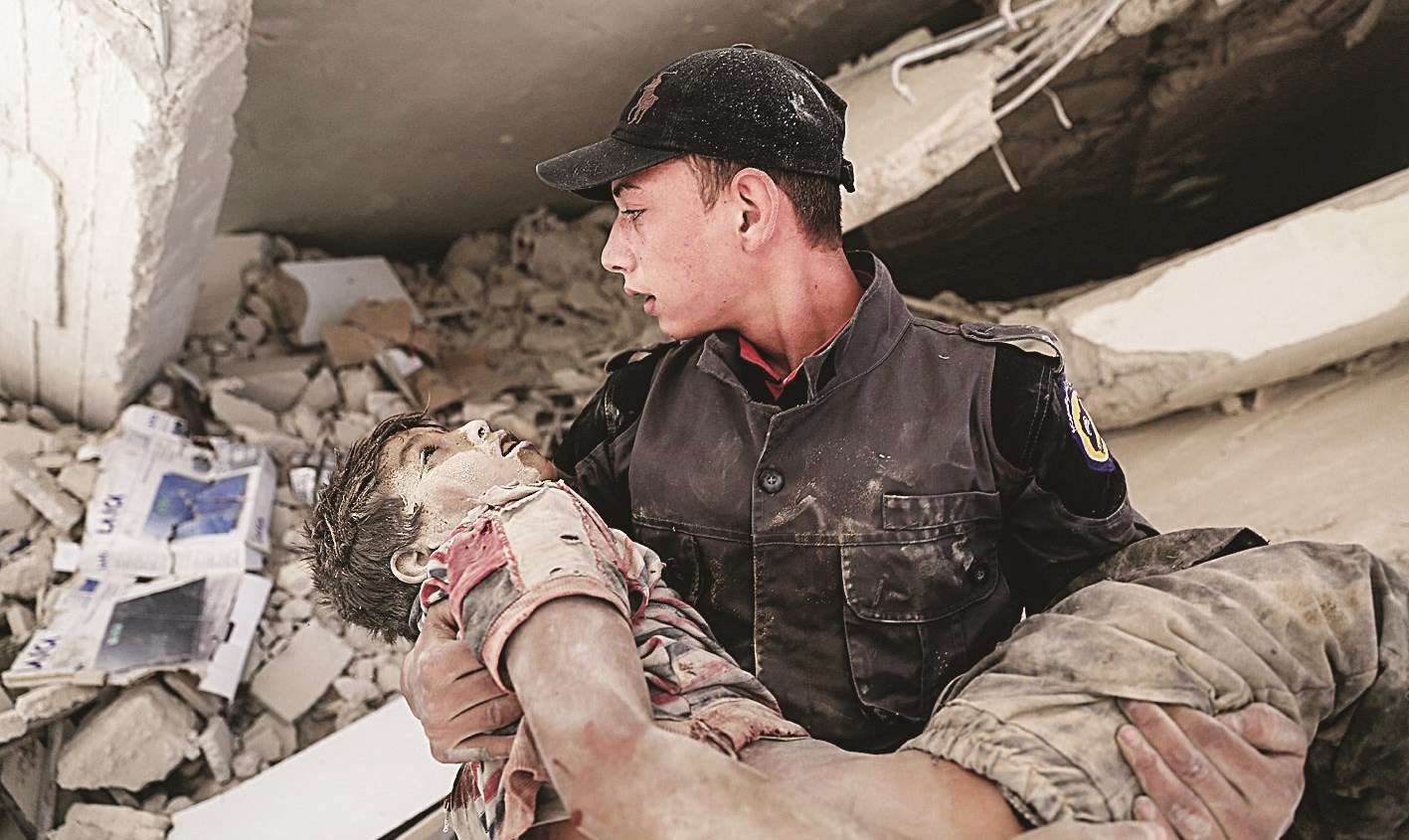 مُسعف يحمل فتى جريحاً انتُشل من تحت أنقاض مبنى في دوما... وفي الإطار جثة أبو هاجر الحمصي (أ ب)