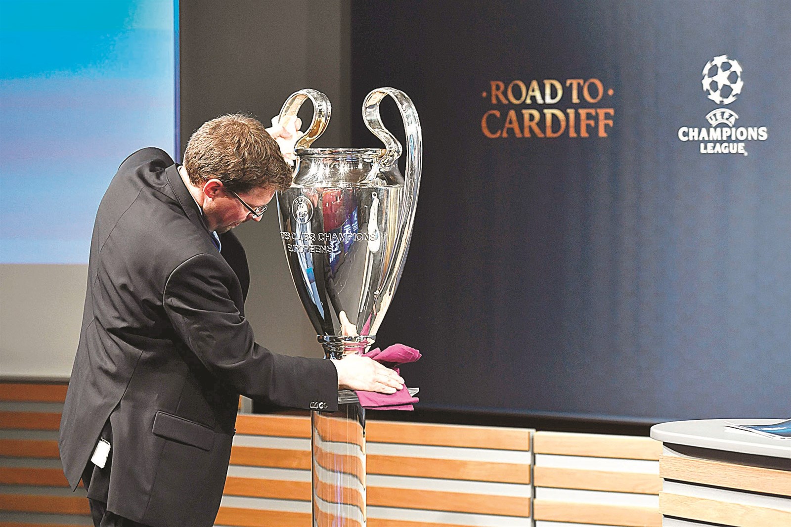 عامل يمسح الغبار عن كأس دوري أبطال أوروبا قبيل انطلاق مراسم القرعة أمس (أ ف ب)