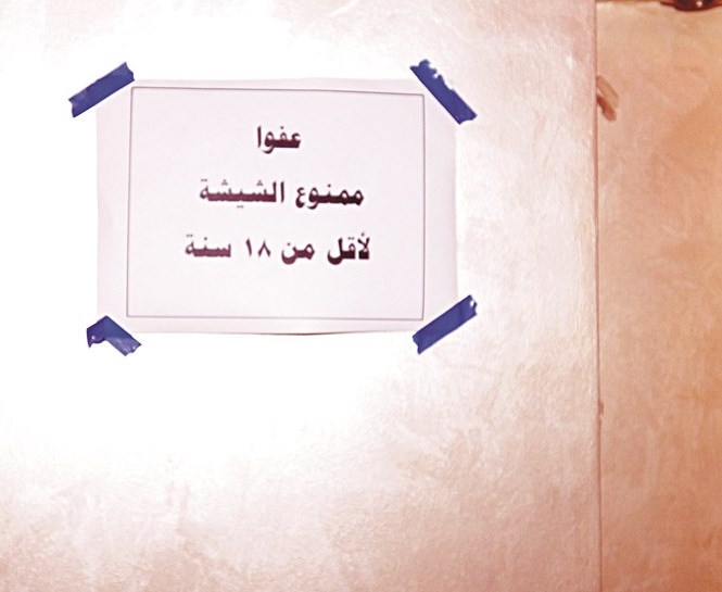 لوحة على جدار مقهى تمنع الشيشة لمن هم دون 18 عاما