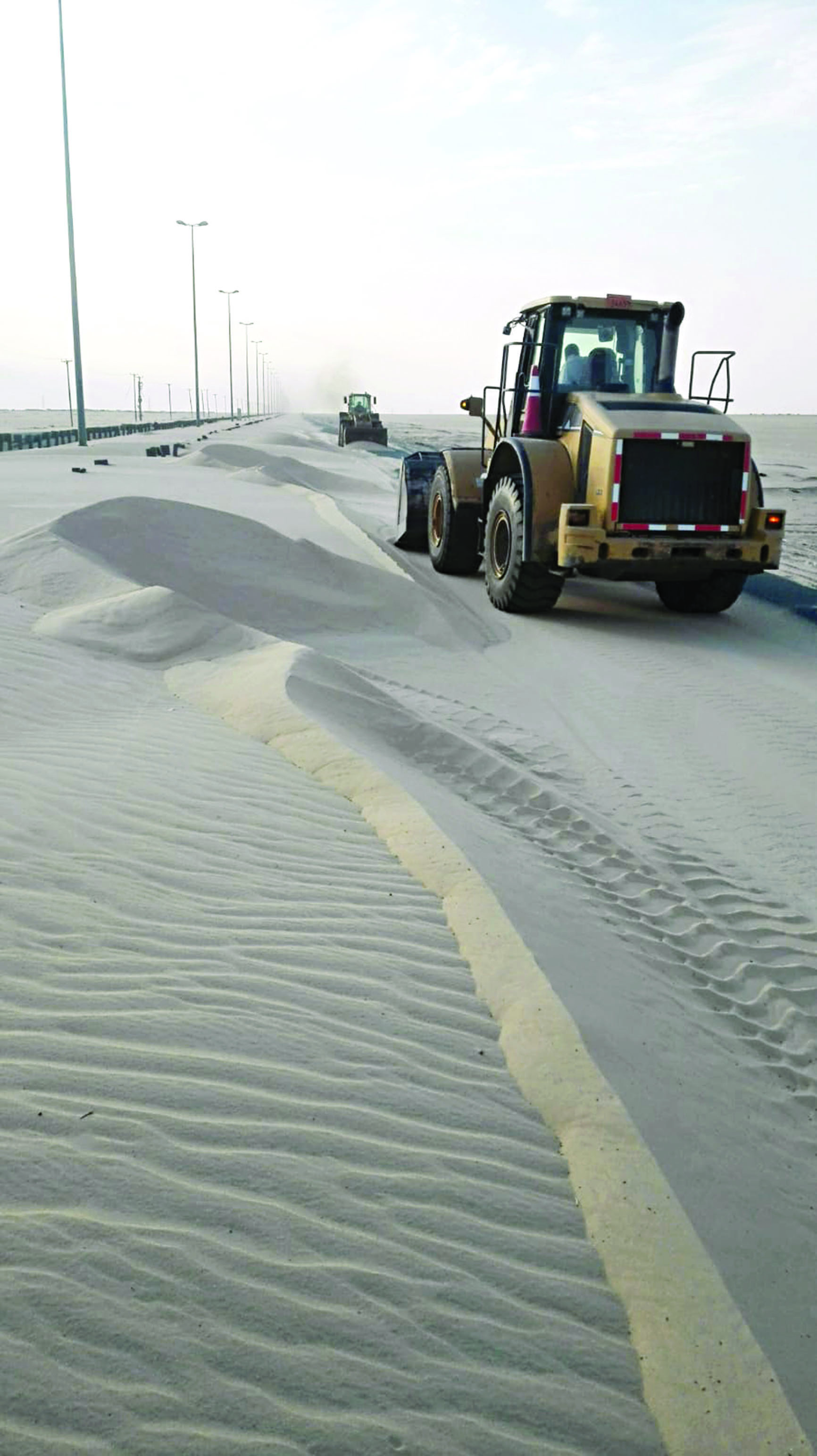 جرافتان ترفعان تلالاً من الرمال عن الطرق