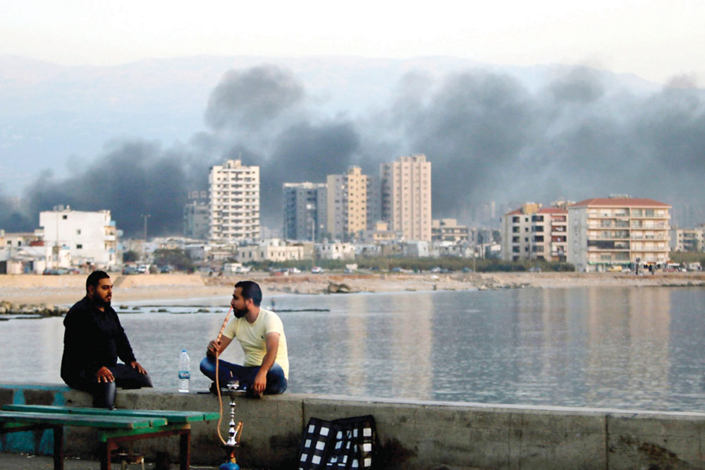 لبنانيان يدخّنان الشيشة بينما يتصاعد الدخان فوق مدينة طرابلس أمس	 (أ ف ب)