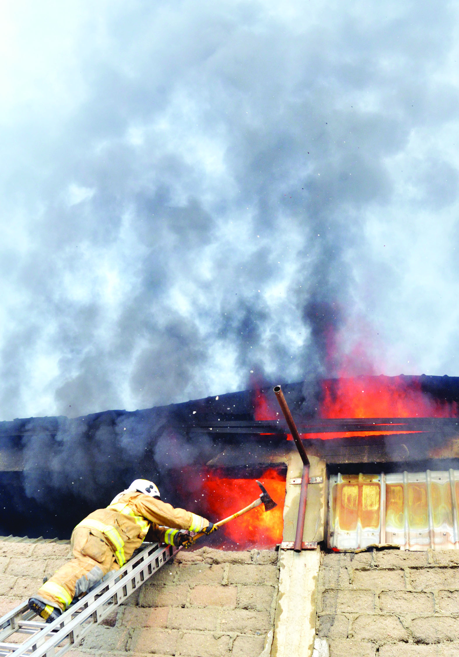 إطفائي يحاول فتح ثغرة إلى داخل المخزن لإطفاء النيران