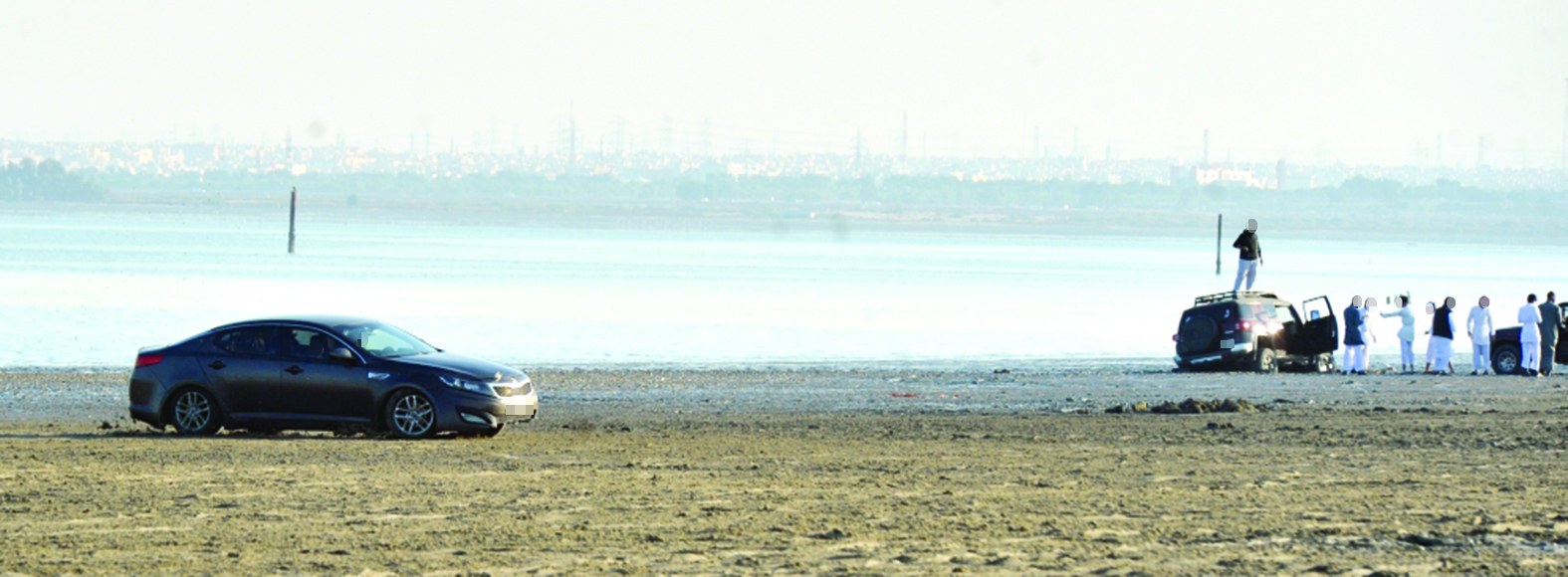 بينما يستعرض أحد المستهترين ينشغل آخرون بسيارة غاصت في الرمال