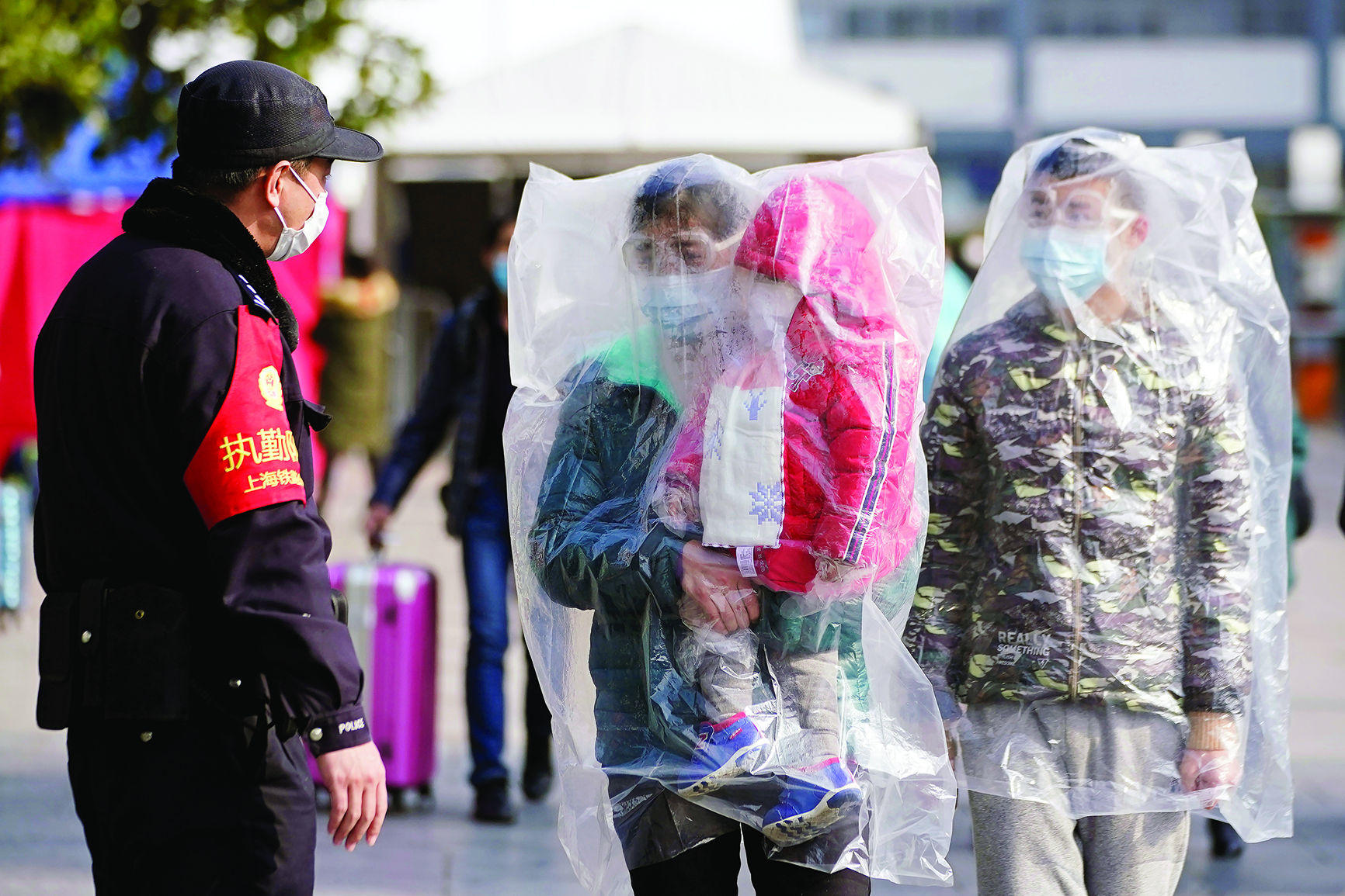 ركاب صينيون يسيرون خارج محطة سكة حديد شانغهاي وهم يرتدون أقنعة ويغطون أجسامهم بأكياس بلاستيكية 