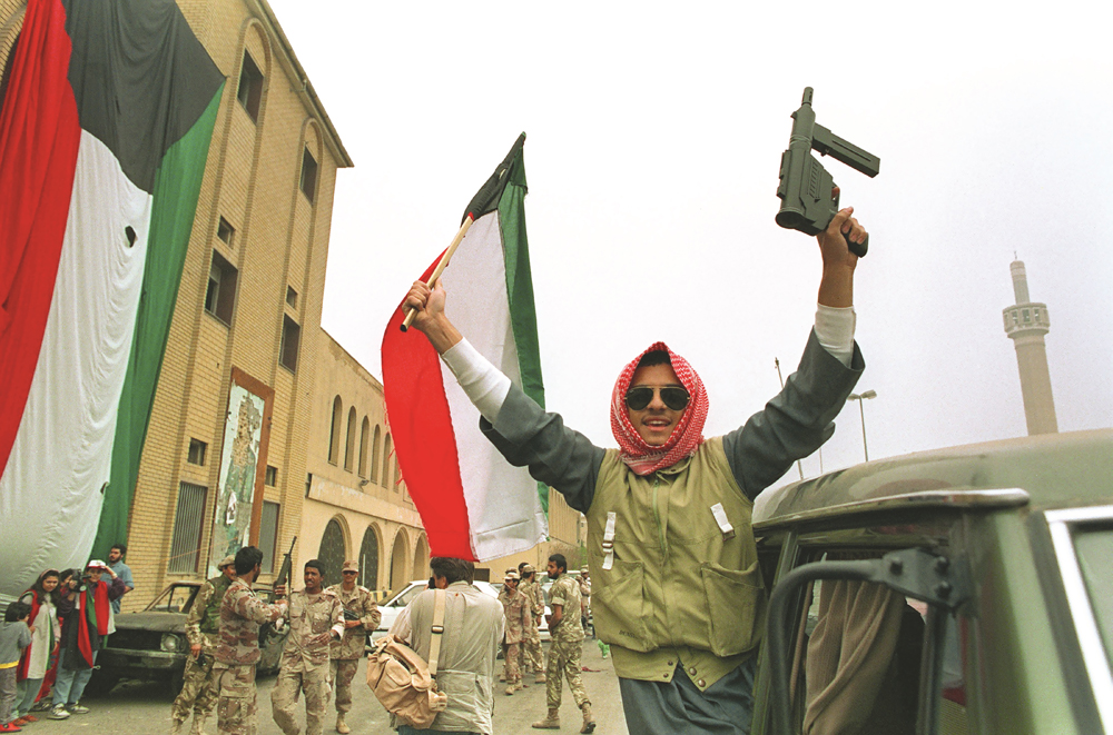 أحد عناصر المقاومة الكويتية يرفع بندقيته والعلم الوطني احتفالاً بالتحرير