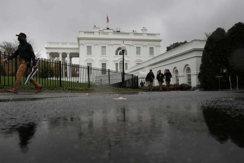 موظفون وصحافيون يمشون عبر درب المرج الشمالي بينما تهطل الأمطار على البيت الأبيض خلال عاصفة في واشنطن أمس (رويترز)