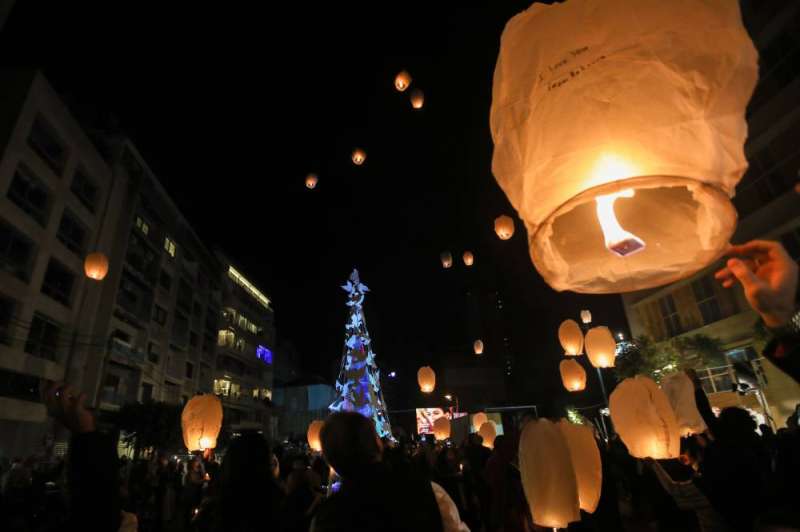 لبنانيون يطلقون فوانيس في حي الجميزة خلال إضاءة شجرة عيد الميلاد تخليداً لذكرى ضحايا انفجار ميناء بيروت (أ ف ب)