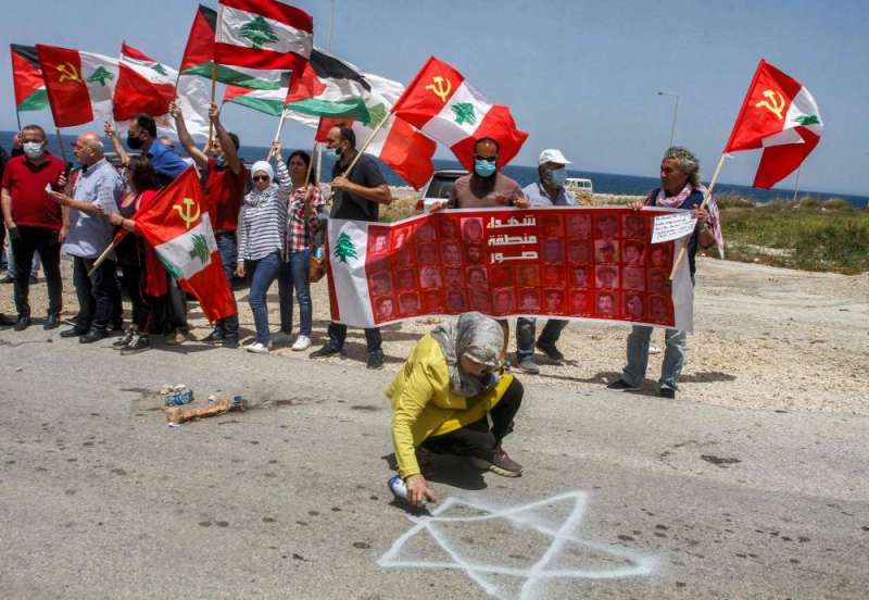 متظاهرة ترسم «نجمة داوود» على الأرض بينما يعتصم أعضاء من الحزب الشيوعي اللبناني على الطريق الرئيسية بالقرب من بلدة الناقورة احتجاجاً على استئناف المحادثات غير المباشرة في شأن ترسيم الحدود البحرية الثلاثاء (أ ف ب)