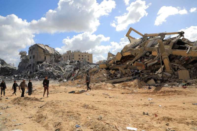 فلسطينيون يسيرون قرب أبراج دمرتها الحرب في خان يونس  (ِشينخوا)