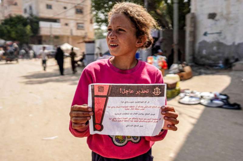 طفلة فلسطينية تحمل منشوراً أسقطه الجيش الإسرائيلي على دير البلح وحذّر فيه من التواجد شمال غزة (أ ف ب)
