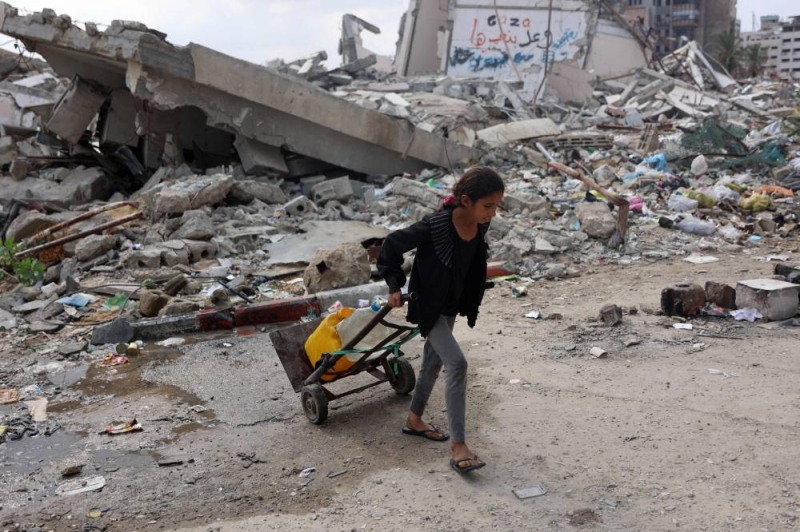 فتاة فلسطينية تنقل المياه لأسرتها وسط الركام شمال غزة أمس (أ ف ب)