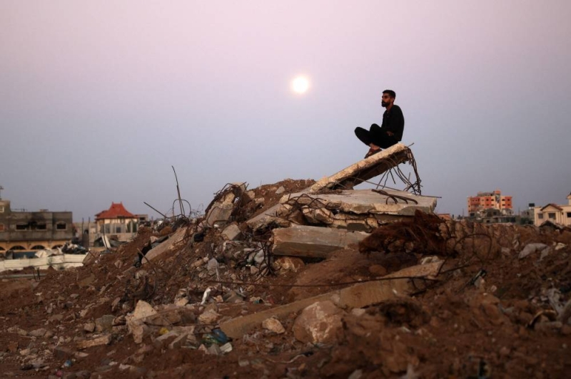 فلسطيني يجلس فوق ركام منزل مُدمّر في مخيم البريج للاجئين وسط غزة (أ ف ب)