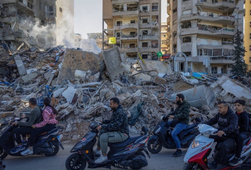 لبنانيون يمرون بدراجاتهم النارية قرب مبنى استهدفته غارات على الضاحية الجنوبية لبيروت (رويترز) 