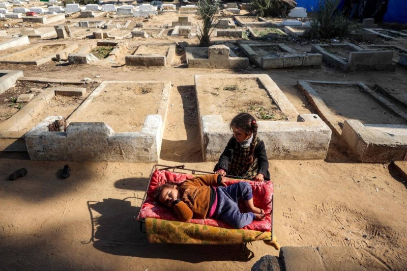 طفلة تجلس بجوار شقيقتها قرب مقابر لجأ إليها نازحون في ديرالبلح وسط غزة (أ ف ب)