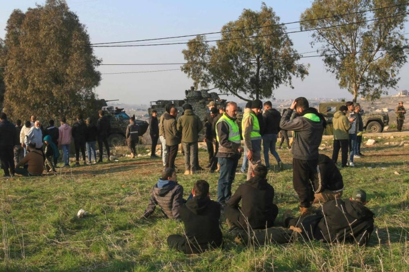 سكان من ميس الجبل ينتظرون في أحد الحقول العودة إلى بلدتهم (أ ف ب)