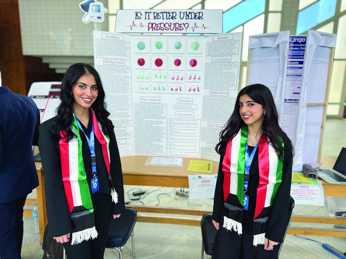 الطالبتان غالية جمال وشيخة الفاضل أمام لوحة عرض مشروعهما خلال المشاركة في المعرض 