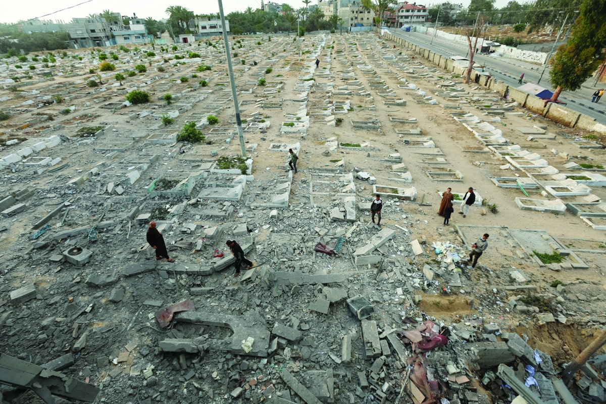 فلسطينيون يتفقدون مقبرة استهدفتها غارات إسرائيلية في ديرالبلح (رويترز)