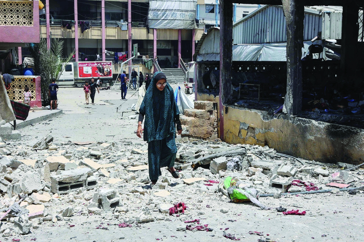 فلسطينية تسير بين أنقاض مدرسة دمّرتها الغارات الإسرائيلية في غزة (أ ف ب)