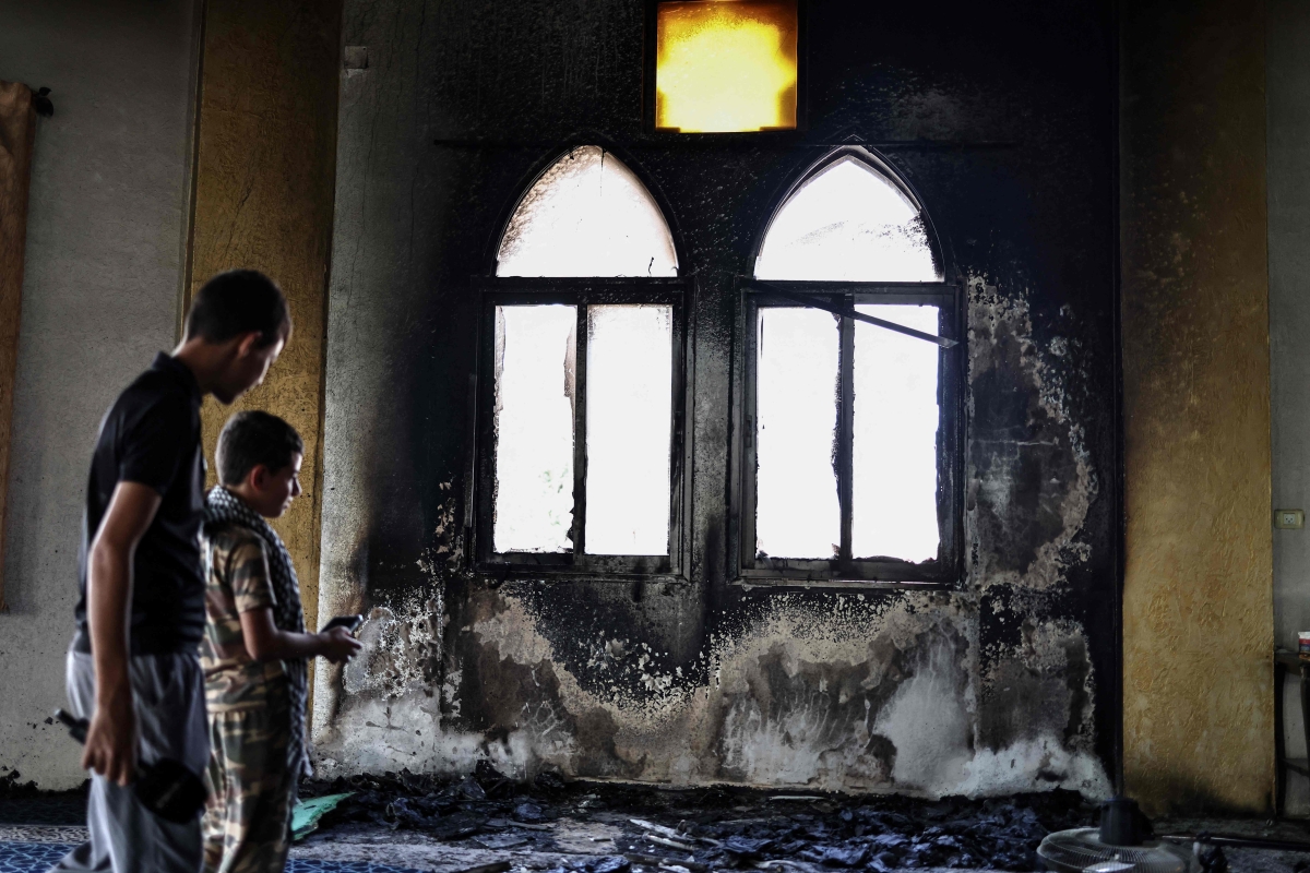 فلسطينيان ينظران إلى أضرار الحريق داخل المسجد (أ ف ب)