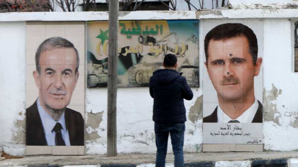 رجل يقف أمام صورة جدارية لبشار الأسد ووالده حافظ في سوريا