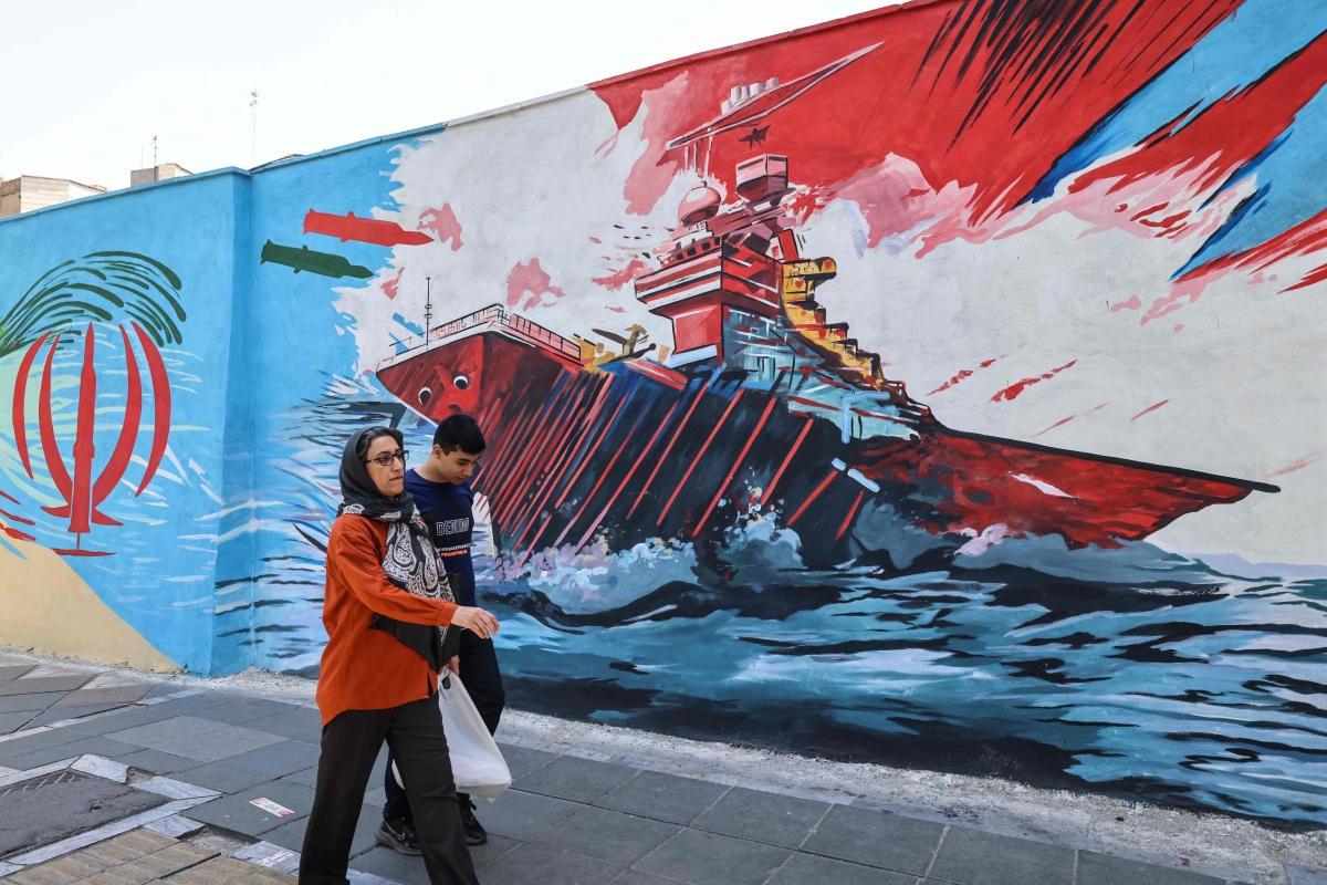 إيرانيان يمران أمام جدارية مناهضة للأميركيين في طهران (أ ف ب)